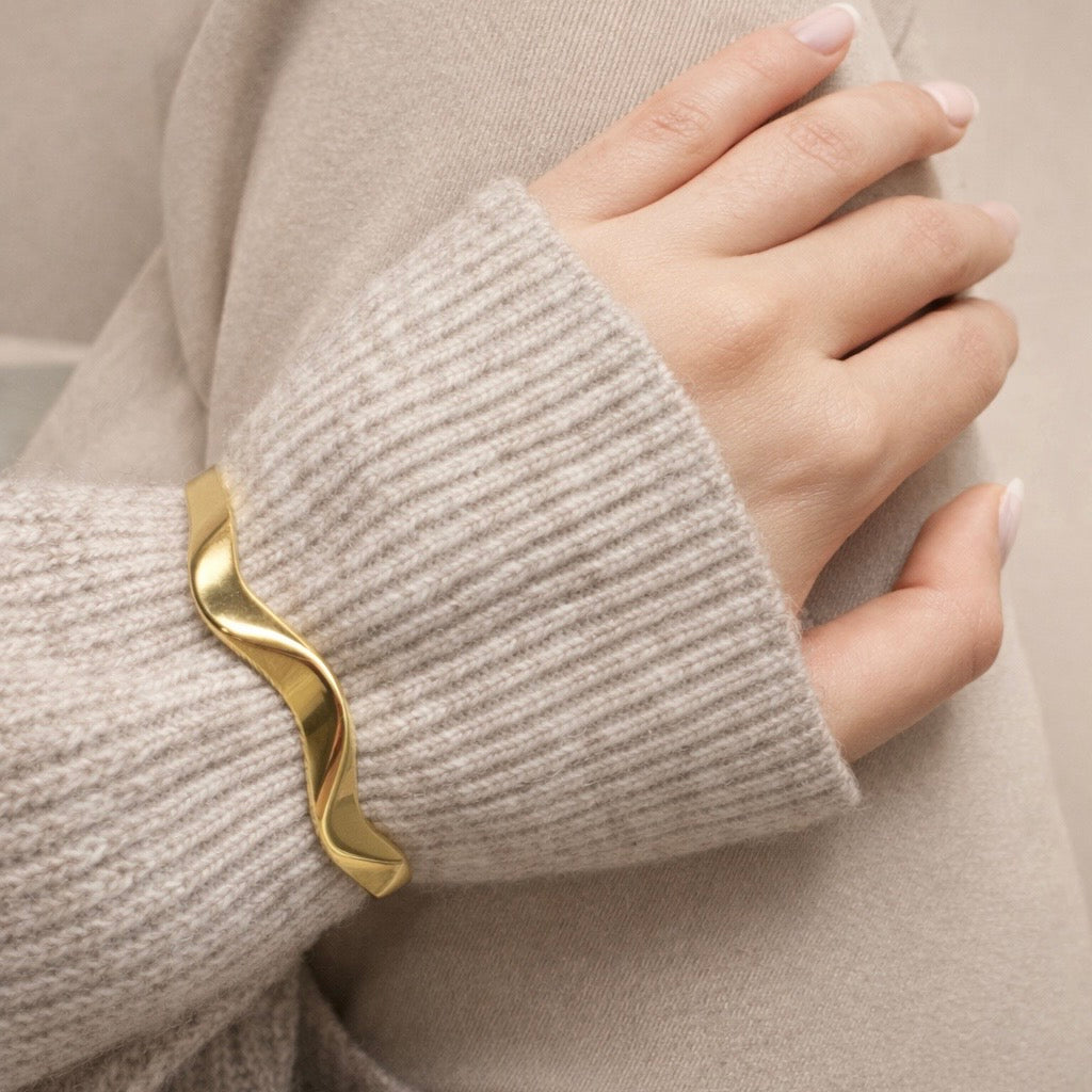Hand wearing LUMHARA wavy 18K gold plated bracelet with neutral knit sleeve