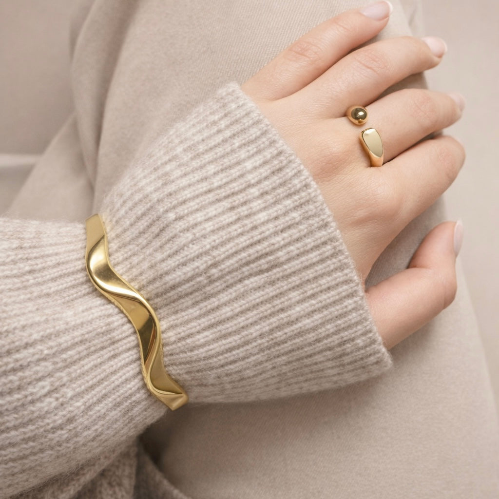 Woman wearing LUMHARA 18K gold plated wave bracelet and modern gold ring on beige knit sleeve