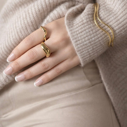 Hand wearing LUMHARA 18K gold plated wavy ring and bracelet, cozy neutral outfit