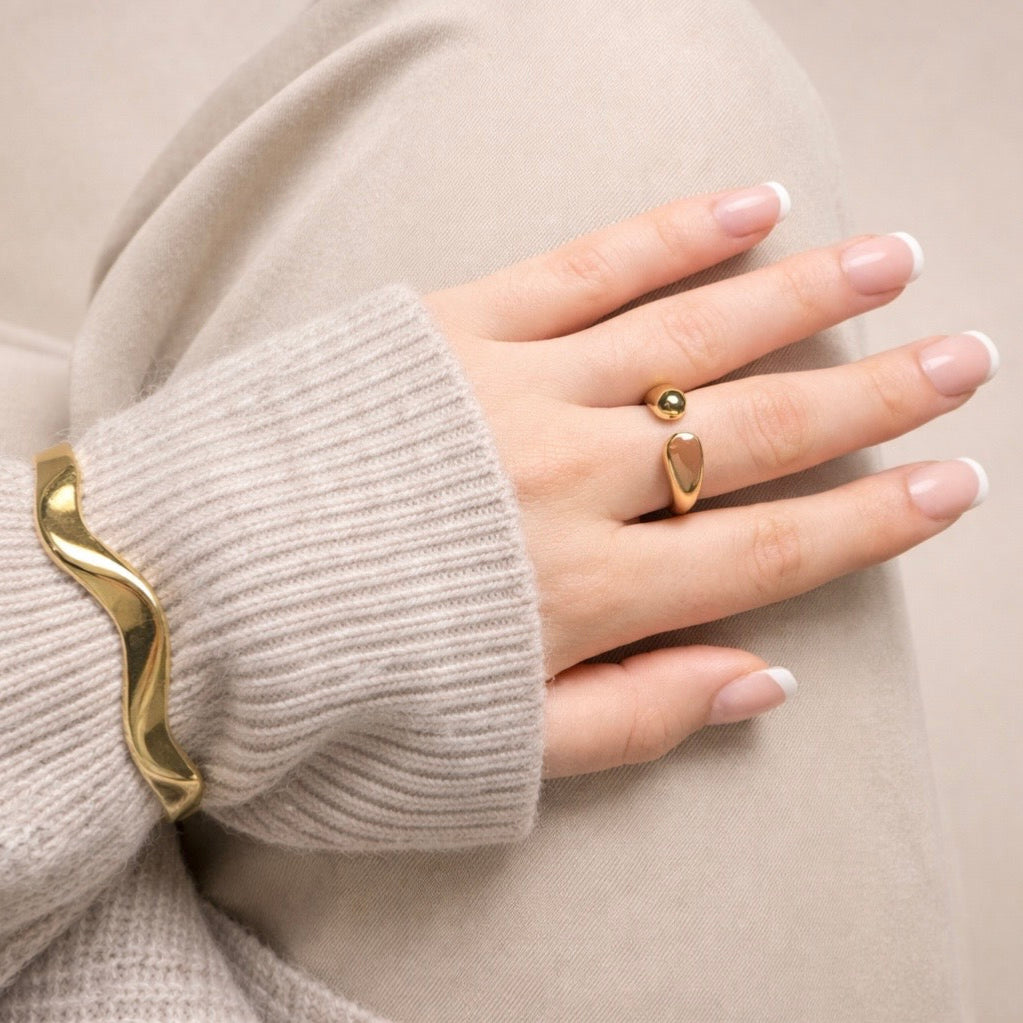 Hand wearing LUMHARA 18K gold plated jewelry, modern ring and wavy bracelet on neutral fabric